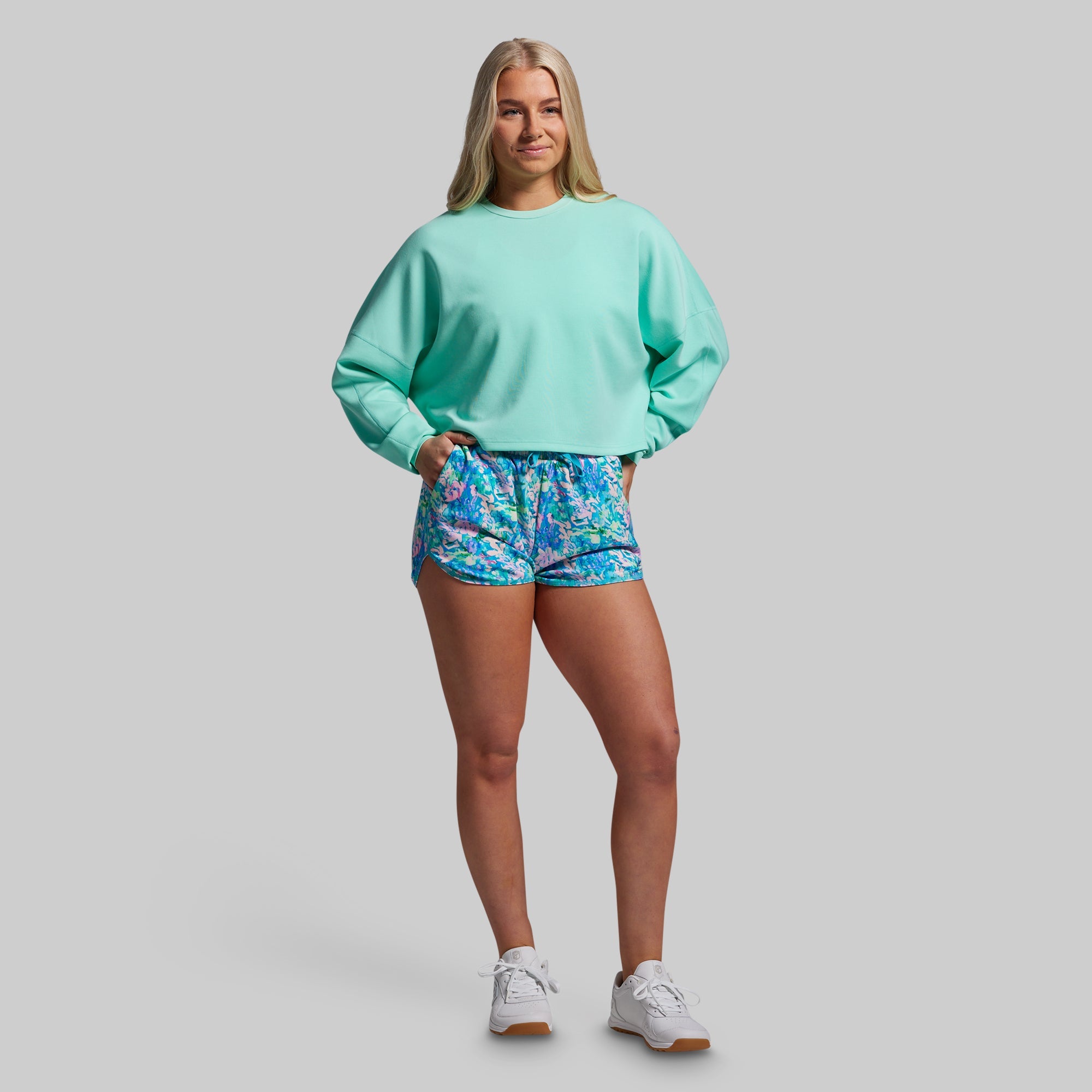Woman wearing a light blue sweatshirt and colorful shorts on a gray background
