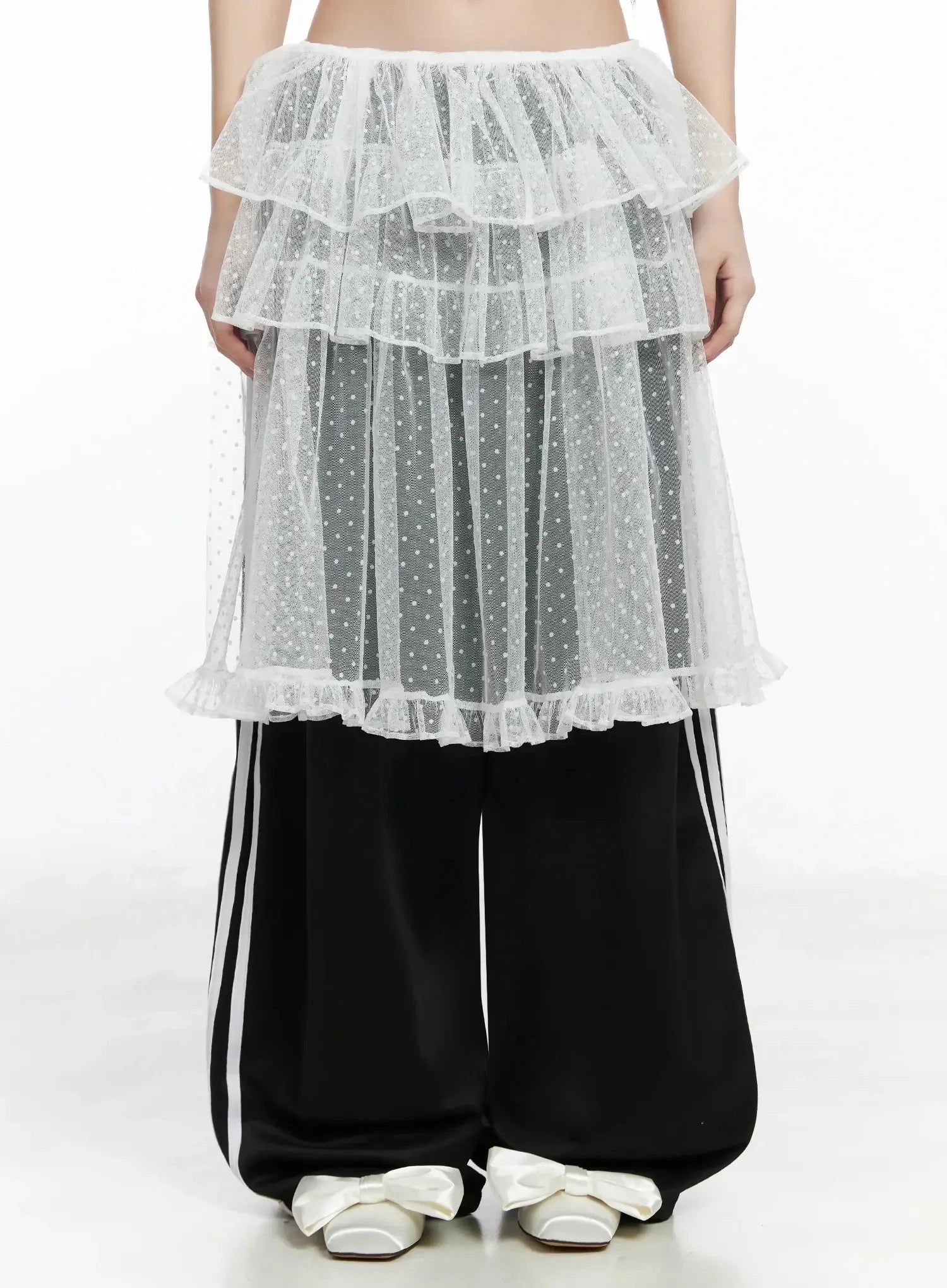 LEWKIN Tiered Tulle Polka Dot Skirt IM506 in white, front view on model, sheer polka dot tulle with multi-tier ruffles and ruffle hem, layered over black track pants with bow flats.