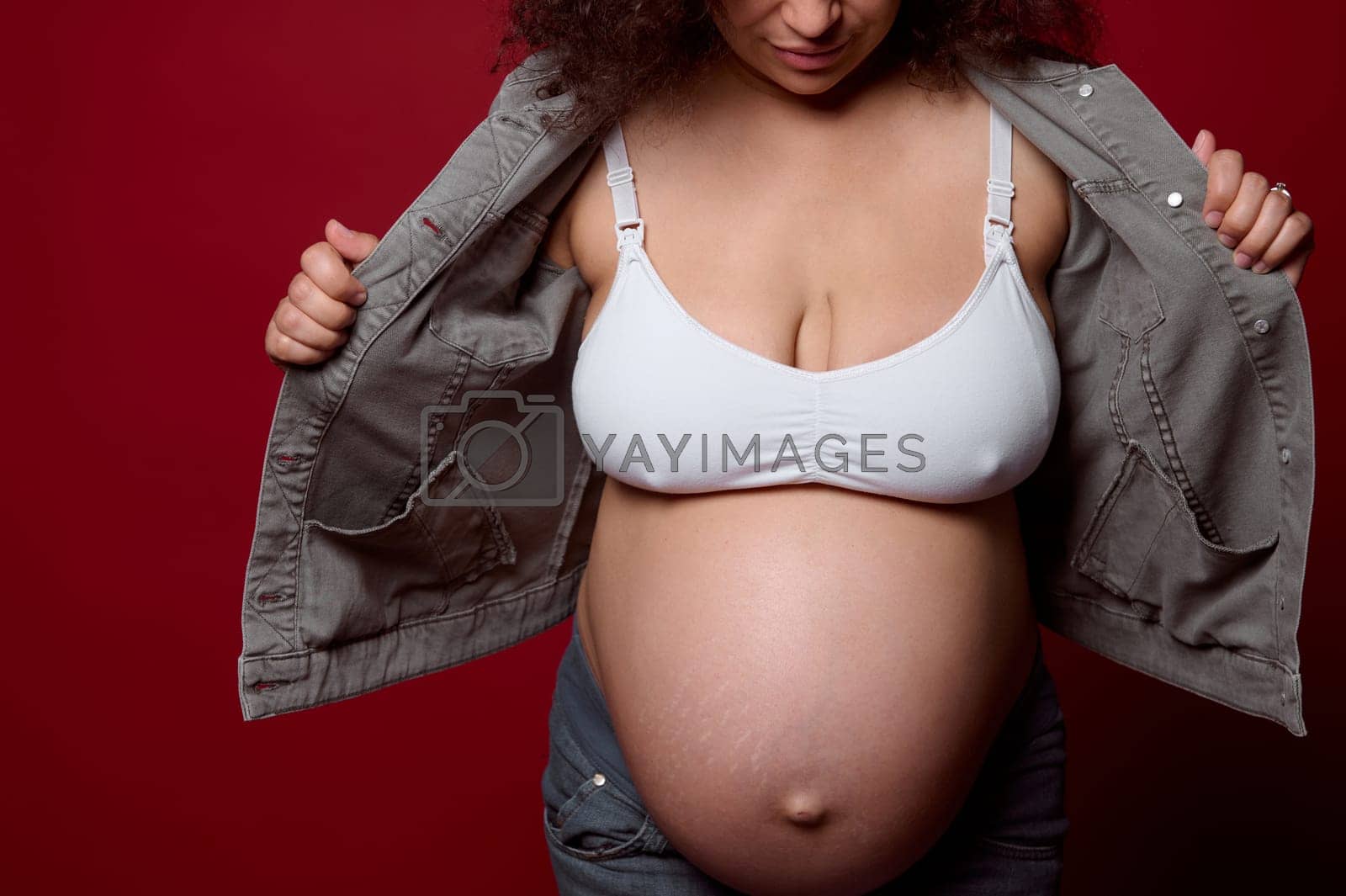Naked belly of a pregnant woman dressed in casual denim clothes, isolated over red studio background by artgf Vectors & Illustrations with Unlimited Downloads