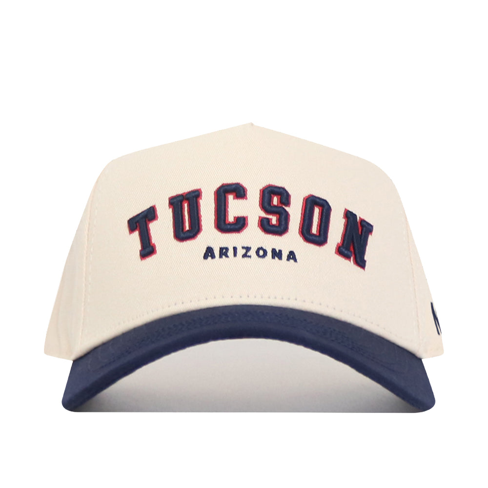 The No Rivals Tucson Hometown Hat is a white snapback with a navy blue brim and “Tucson Arizona” embroidered in bold navy and red. Its structured fit and cotton fabric deliver classic comfort and style.