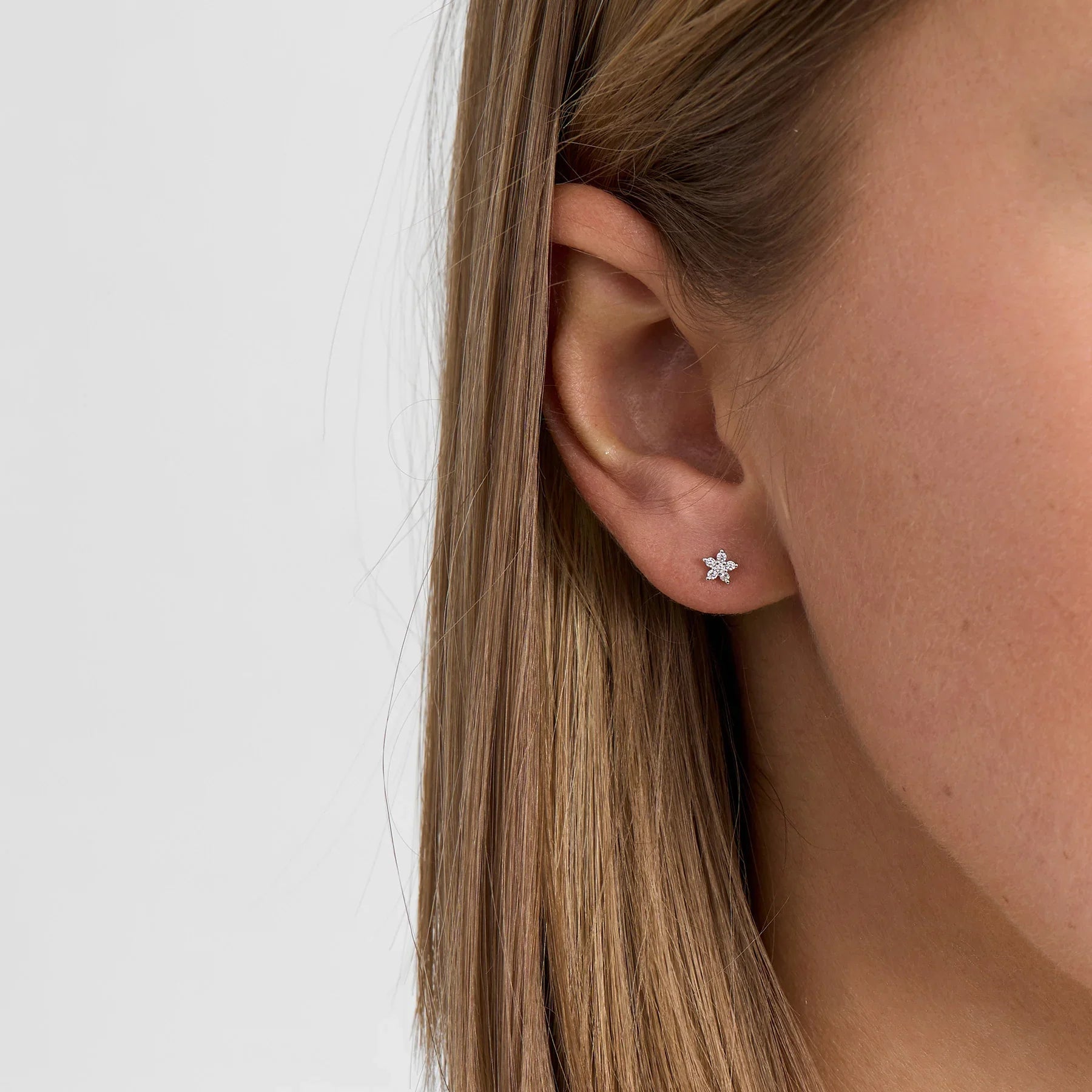 Earrings in silver with flower shape and clear stones, shown on ear, front