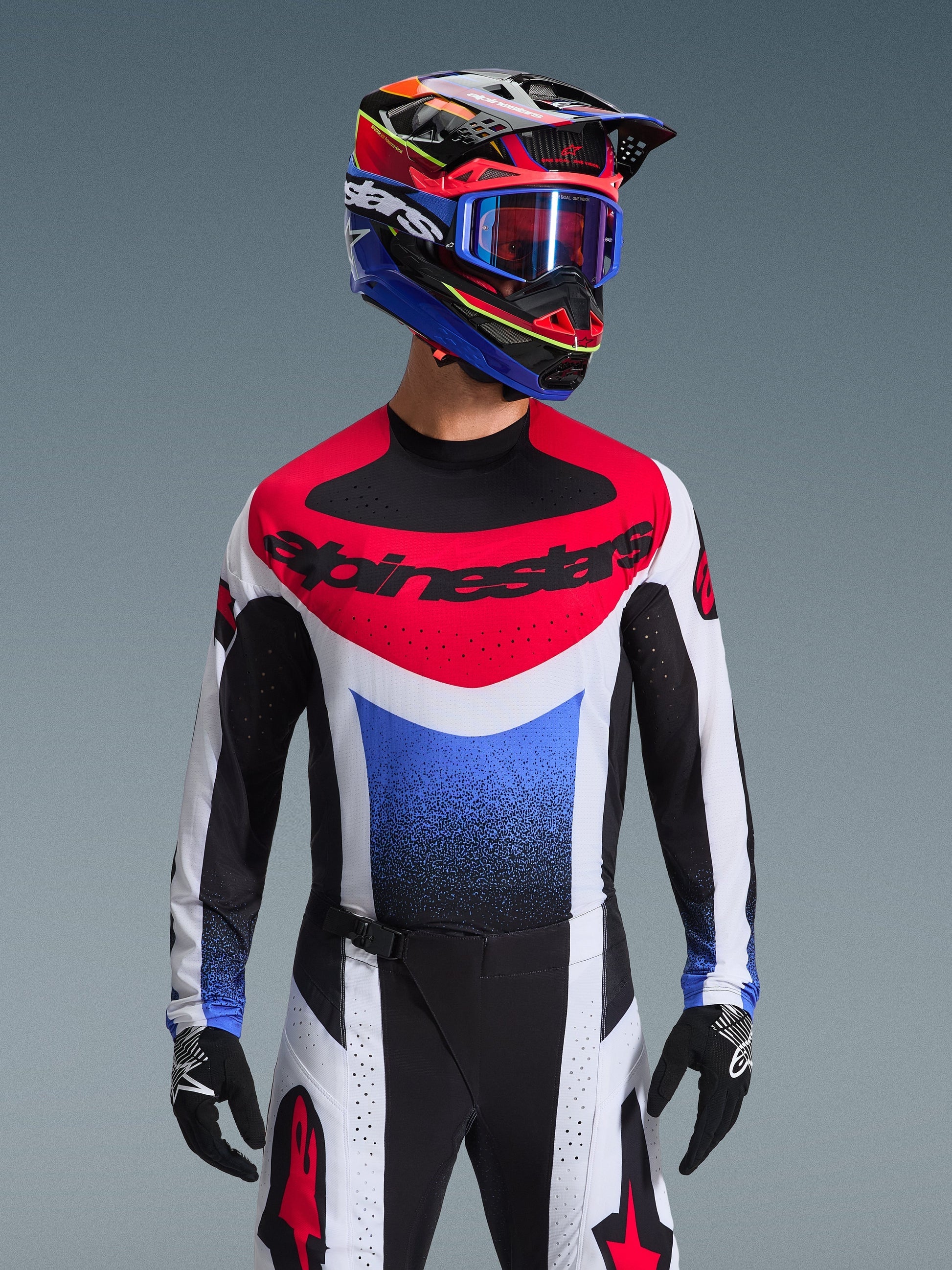 Alpinestars 2026 Techstar Knif Jersey, motorcross shirt, rood wit en blauw, met een opvallend borstlogo en kleurverloop op de romp, gedragen door een rijder met een bijpassende veelkleurige helm, blauwe crossbril en zwarte handschoenen, professionele off-road race-uitrusting