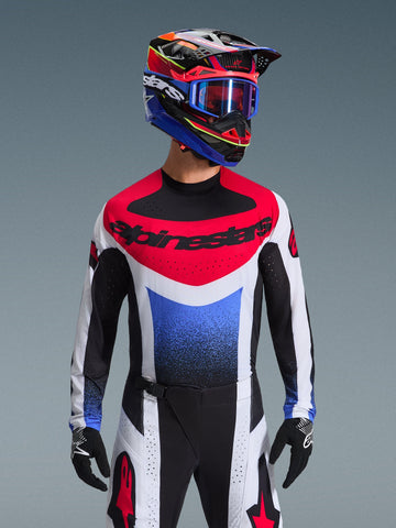 Alpinestars 2026 Techstar Knif Jersey, motorcross shirt, rood wit en blauw, met een opvallend borstlogo en kleurverloop op de romp, gedragen door een rijder met een bijpassende veelkleurige helm, blauwe crossbril en zwarte handschoenen, professionele off-road race-uitrusting