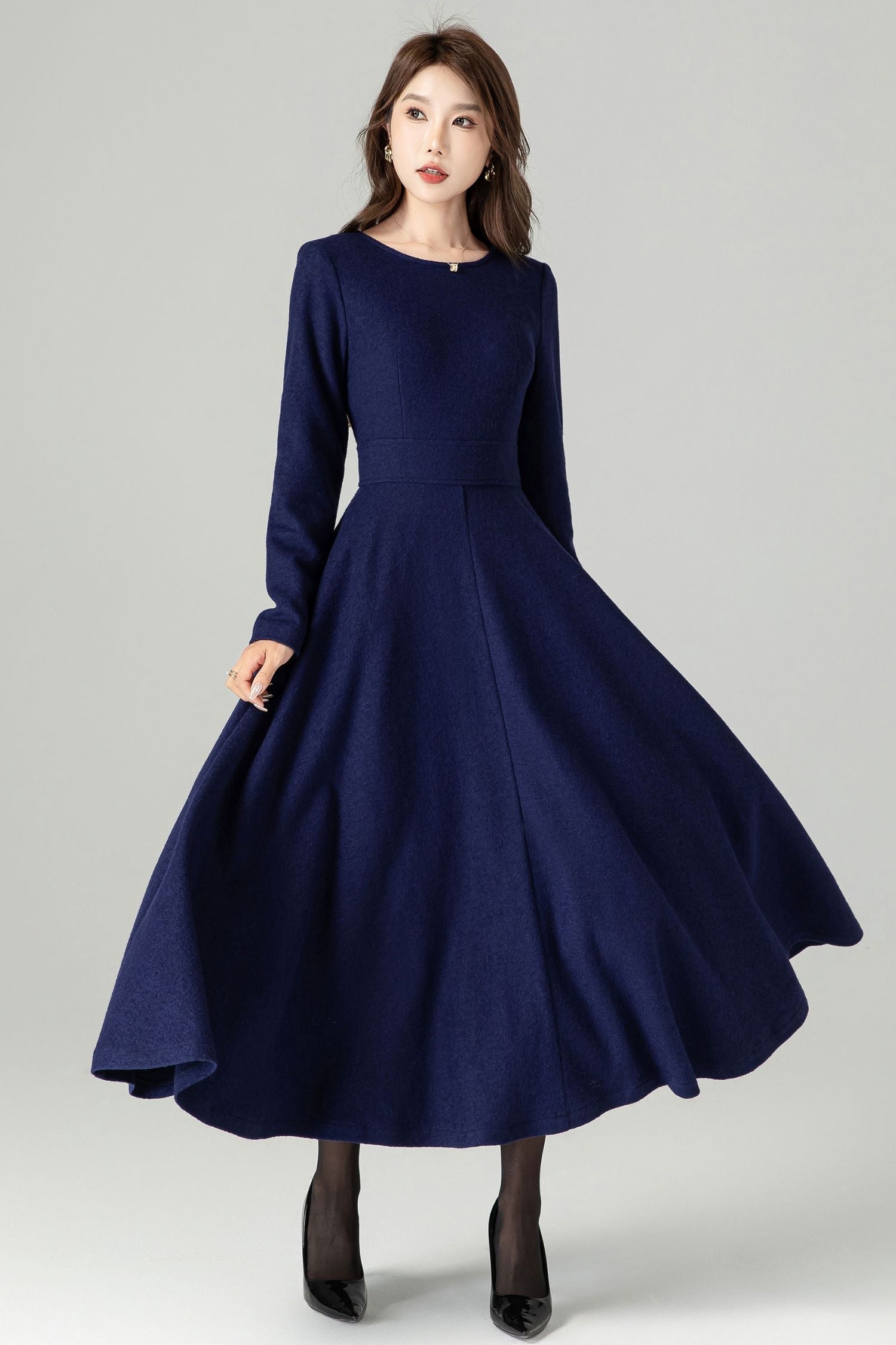 A woman wearing a long sleeve, midi length navy wool dress with a round neckline, fit and flare silhouette, and back zipper closure.
