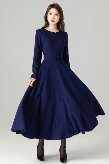 A woman wearing a long sleeve, midi length navy wool dress with a round neckline, fit and flare silhouette, and back zipper closure.