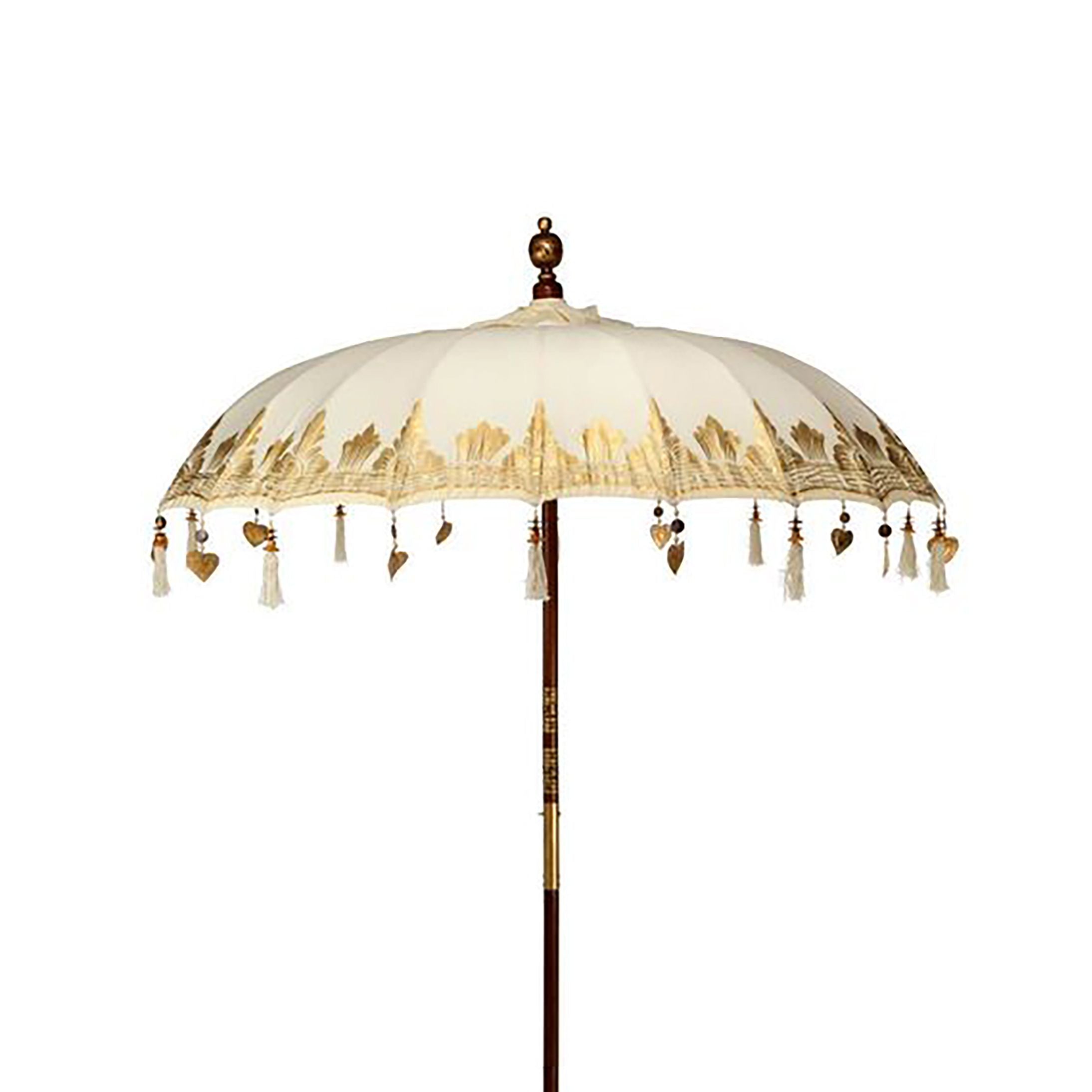 Sombrilla de patio estilo Bali en lona color crema con detalles dorados, flecos y poste de madera sobre fondo blanco