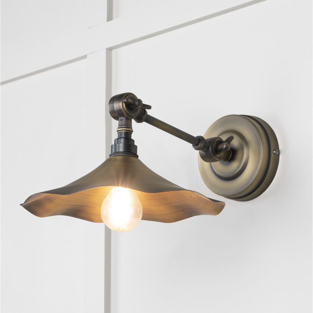 Brushed aged brass flora wall light against a white panelled wall