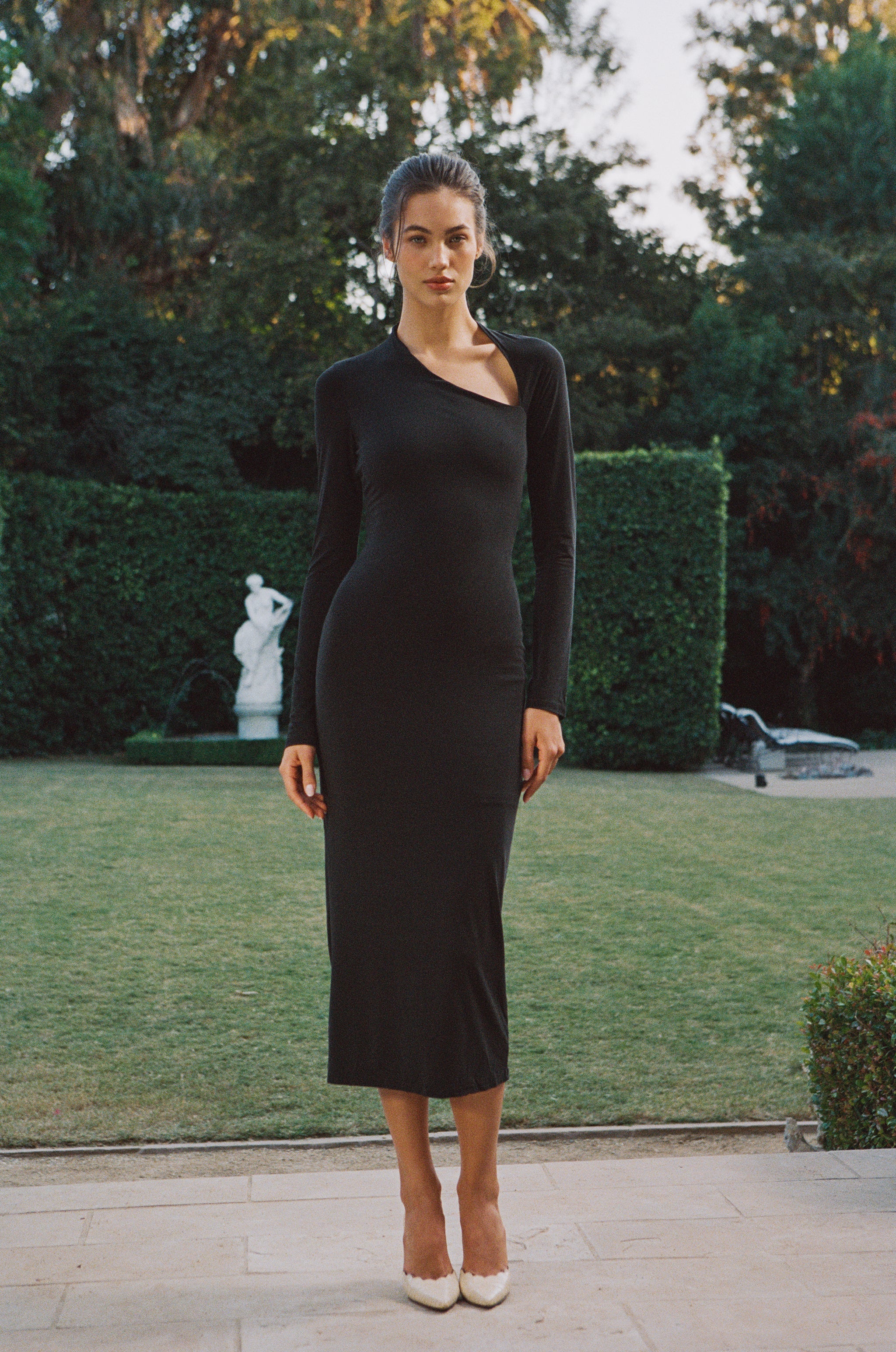 Black Celia full-length long-sleeve dress with a front cutout slit at the neck, worn by a model outdoors.